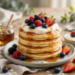 Stack of fluffy protein pancakes topped with fresh berries and maple syrup on a white plate