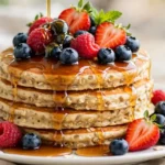 Stack of fluffy protein pancakes topped with fresh berries and maple syrup on a white plate